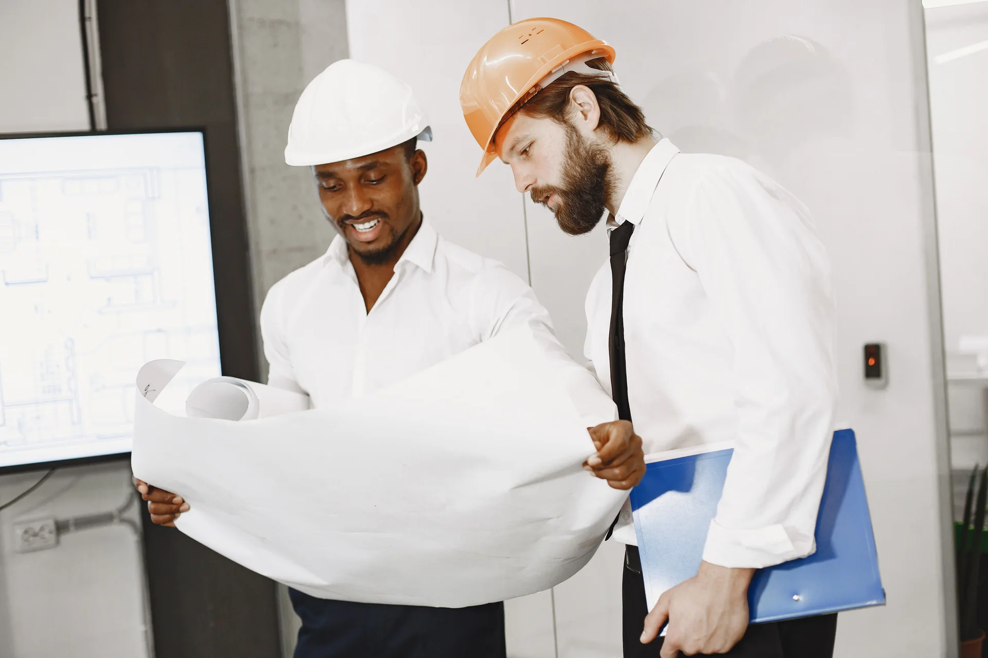 Two engineers wearing hard hats reviewing construction drawings
